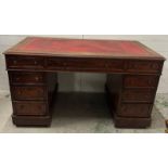 A red leather topped pedestal desk with a central long drawer flanked by four drawers on either side