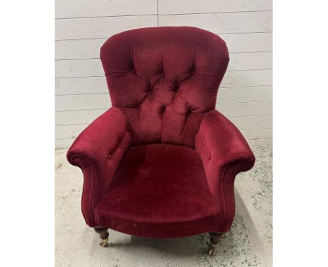A burgundy upholstered button back arm chair on castors 