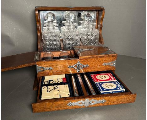An oak three bottle tantalus and games compendium with heavy shot glasses, chess pieces and dominos