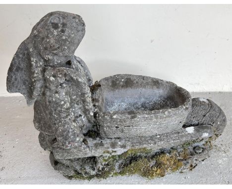 A weathered concrete garden planter modelled as a rabbit pushing a wheel barrow. Approx. 40cm tall x 47cm long. 