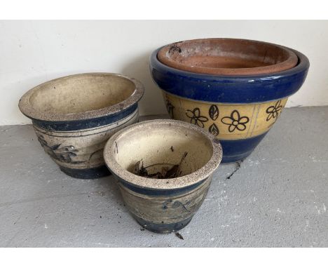 3 modern garden planters of varying sizes, blue banded glaze with floral details. Largest pot has a smaller terracotta plante