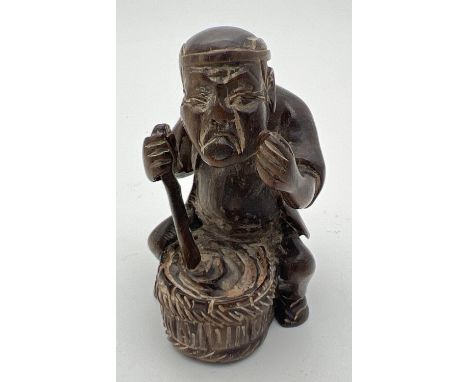 A carved wooden netsuke modelled as a man stirring a pot. Set with small mother of pearl disc to underside. Approx. 5cm tall.
