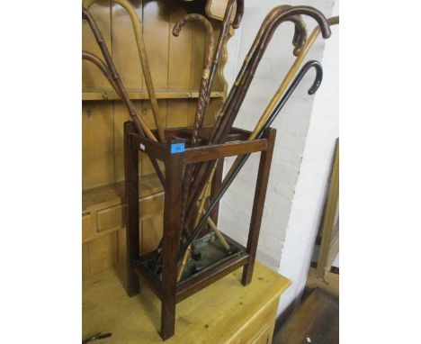 An early 20th century oak stick stand with mixed walking sticks, to include one with a yellow metal band 