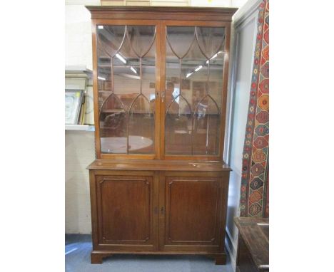 A reproduction of a George III mahogany bookcase having astrigal glazed doors above two cupboard doors and standing on bracke