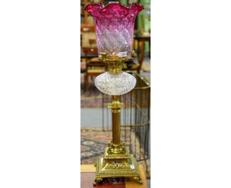 An Elaborate Brass Column Oil Lamp, cranberry etched shade, clear glass reservoir, square base scroll supports, pierced and f