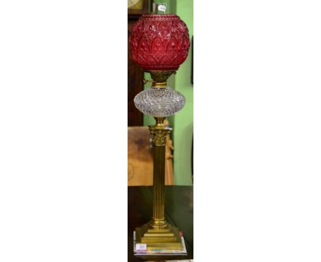 A Brass Corinthian Column Oil Lamp, with cranberry globular glass shade moulded with fleur de lys motifs, clear glass reservo