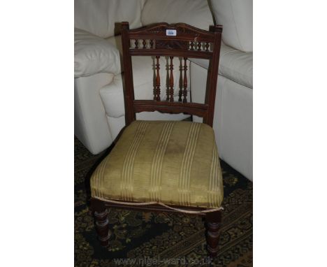 A Victorian low walnut framed Nursing Chair having carved top rail on spindle turned supports with carved central panel on th