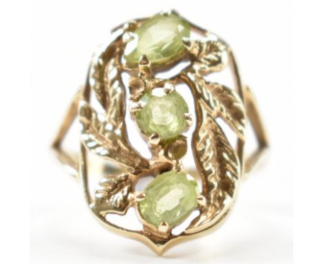 A gold and peridot dress ring. The ring having a central round cut green stone flanked by an oval cut and pear cut peridot he