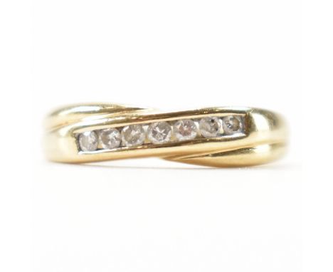A gold and diamond crossover ring. The ring having a central row of seven round cut diamonds and a crossover band. Marked 375