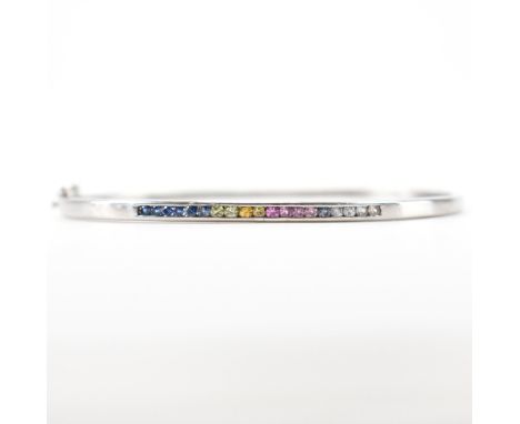 A hallmarked 9ct white gold and coloured stone bangle bracelet. The bracelet being channel set with multi coloured stones. Ha