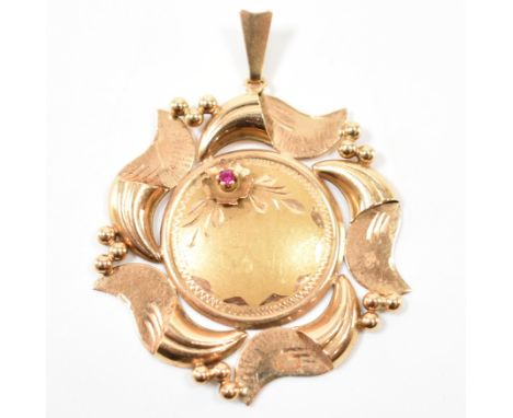 A gold Argentinian necklace pendant having a central round cut ruby within a claw setting with incised decoration and scrolle