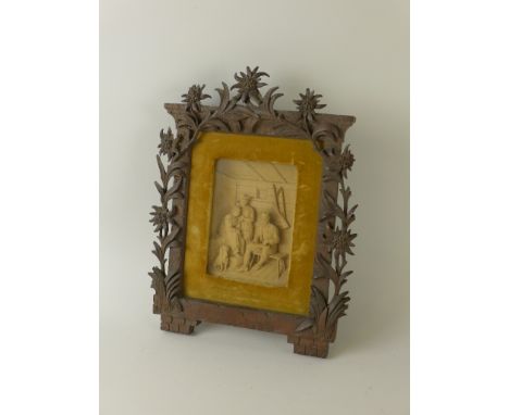 A German carved Frame containing an interior relief figure group of a man playing a musical instrument and a dog sat at their