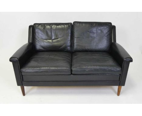 A 1960s Danish black leather two-seater sofa, having squab cushion backs and seats, raised on turned teak supports, w.132cm