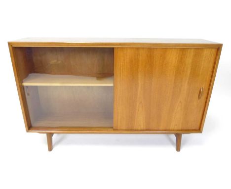 Herbert E Gibbs - a 1960s teak low bookcase, having single glazed sliding door and single panelled door, raised on curved tap