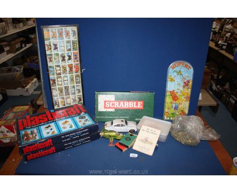 A box of games including Scrabble, Rupert bagatelle, Beatrix Potter phonetic book, old Police jaguar car, etc.