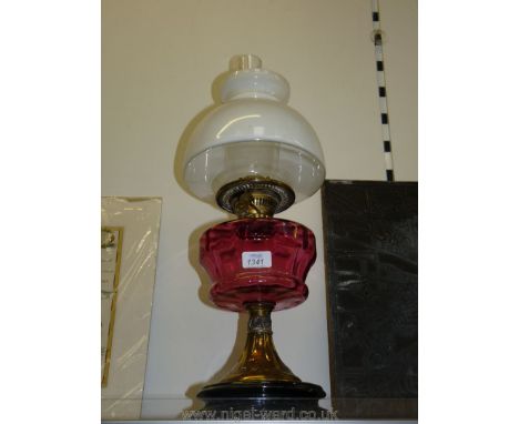 An oil lamp with a cranberry glass reservoir and white glass shade.