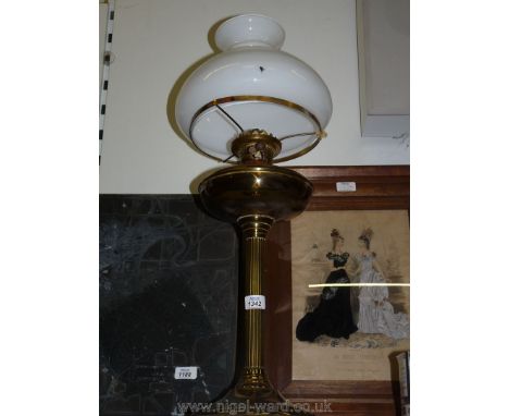 An oil lamp with a tall brass reeded column base and reservoir with a white glass shade.