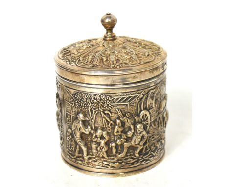 A white metal canister type tea caddy with relief decoration of countryside working scenes, height 11cm.