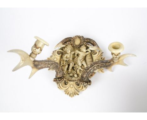A 1920's ceramic wall sconce, designed as two putti seated on a branch within a central cartouche surrounded by leaves, the c