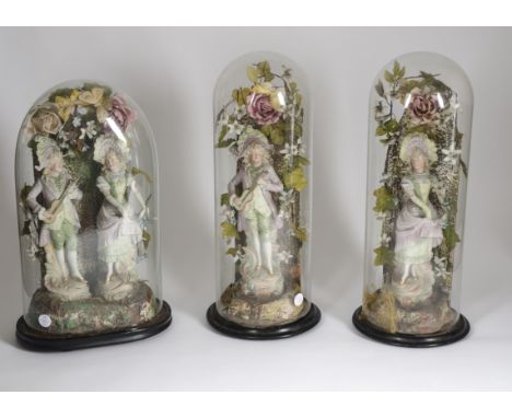 Three ceramic models of men and women, placed within naturalistic settings underneath glass domes on wooden circular bases, h
