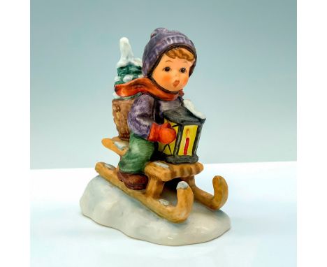 A figure of a young child in a blue jacket and hat with green pants sliding down a snowy hill on a sled. Goebel Hummel backst