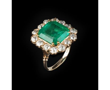 AN EMERALD AND DIAMOND CLUSTER RING, the rectangular step-cut emerald with truncated corners, in double four claw setting, fr