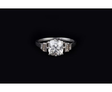 A DIAMOND SINGLE STONE RING, the cushion-shaped old-cut diamond in eight claw setting, between stepped baguette-cut diamond s