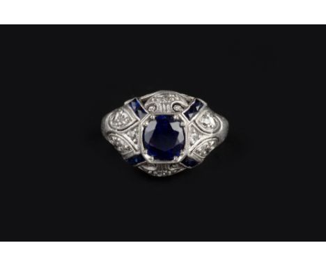 A SYNTHETIC SAPPHIRE AND DIAMOND BOMBE DRESS RING, centred with an oval mixed-cut synthetic sapphire, within a scroll pierced