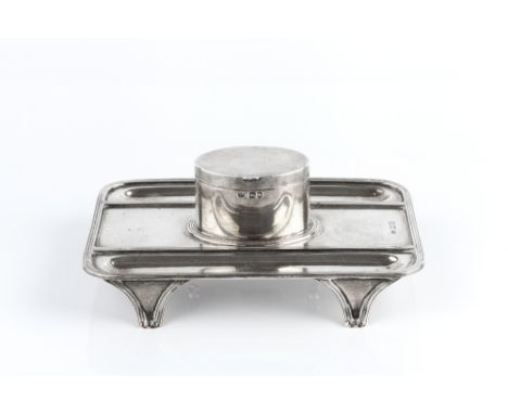 AN EDWARDIAN SILVER INK STAND, with central oval hinged inkwell with removable glass liner, flanked by pen recesses, within r