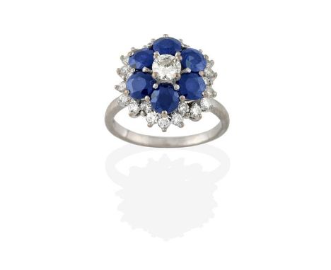 A Sapphire and Diamond Cluster Ring, the central raised round brilliant cut diamond in a border of round cut sapphires, to a 