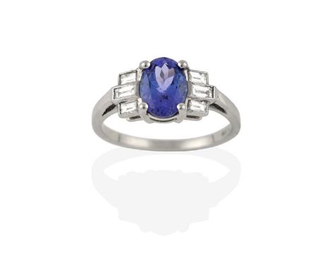 An Art Deco Style Tanzanite and Diamond Ring, the oval cut tanzanite in a white claw setting, flanked by trios of baguette cu