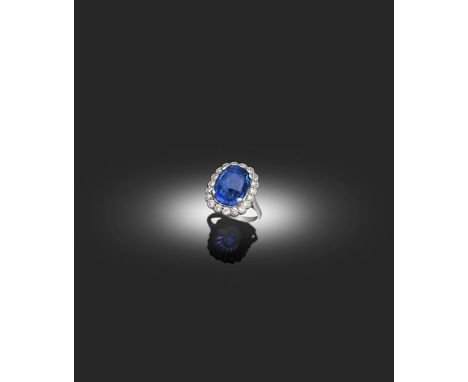 A Sapphire and Diamond Cluster Ring, the oval mixed cut sapphire in a white claw setting, within a border of round brilliant 