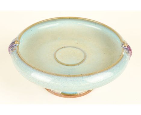 A CHINESE JUN- STYLE HIGH FOOTED SHALLOW BOWLCovered in a light blue glaze and with moulded purple splashed fish handles, 18c