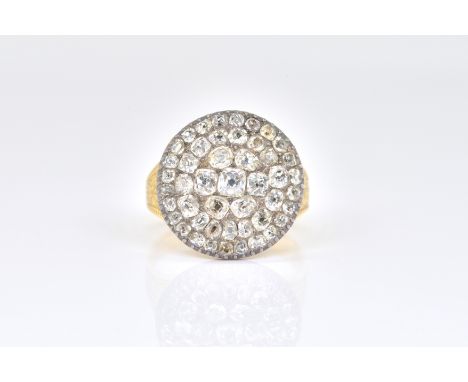 A DIAMOND CIRCULAR CLUSTER RINGIn a gold and silver setting, mounted with variously cut cushion shaped diamonds, between flor