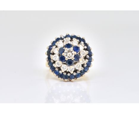 A GOLD, SAPPHIRE AND DIAMOND CLUSTER RINGIn a tiered circular design, claw set with the principle circular cut diamond at the