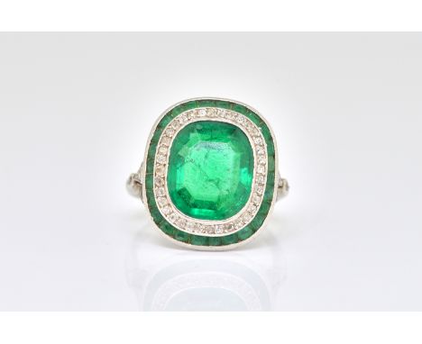 AN EMERALD AND DIAMOND OVAL RINGCirca 1920s, the cushion-cut emerald in a rub-over setting within a border of rose-cut diamon