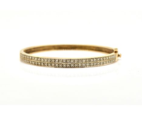 A 9CT GOLD AND DIAMOND BANGLEOf oval hinged form, the front mounted with two rows of circular cut diamonds, on a snap clasp, 