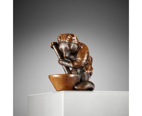 ITSUMIN: A WOOD OKIMONO NETSUKE OF A TANUKI STIRRING MISO IN A MORTARBy Hokyudo Itsumin, signed Itsumin 逸民 to 刀Japan, Tokyo, 