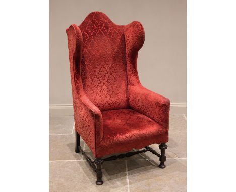 A William and Mary style wing back armchair, early 20th century, in embossed red foliate fabric, the camel back extending to 