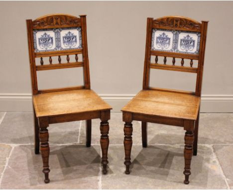 A pair of Victorian golden oak tile back hall chairs, each chair with a foliate carved top rail above two blue and white tile