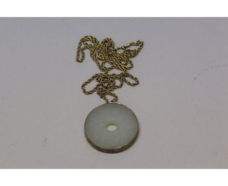 A Chinese carved pale celadon jade bi disc, 4.2cm diameter, within a pierced gilt mount, the lanyard stamped '14k', with yell