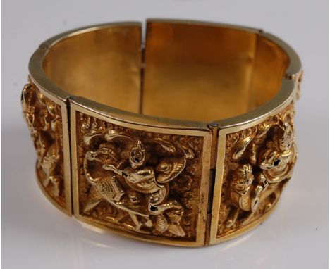 A yellow metal Asian style panel bangle, depicting six embossed sections featuring figures astride various animals, with a bo