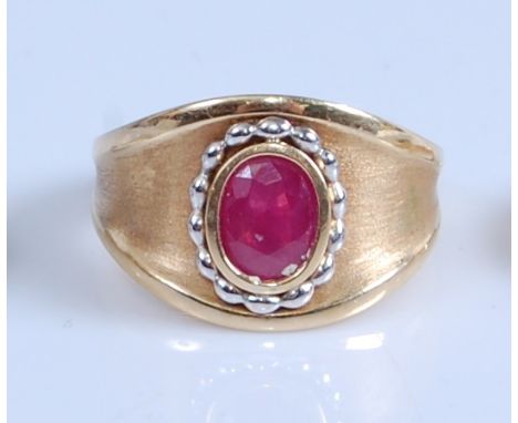 A yellow metal ruby set heavy dress ring, featuring an oval faceted ruby within a yellow and white beaded bezel setting, ruby