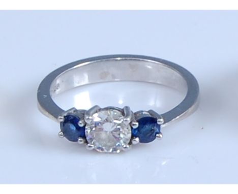 A platinum, diamond and sapphire three-stone ring, featuring a centre round brilliant cut diamond with a round faceted sapphi