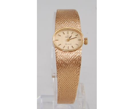 A 9ct yellow gold lady's manual wind Omega DeVille wristwatch, having an oval champagne baton dial and an integral Milanese b