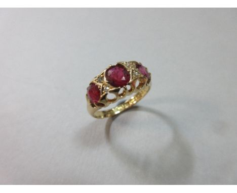 A late Victorian three stone ruby ring with diamond highlights set in 18ct gold, the three graduated oval cut rubies with pai