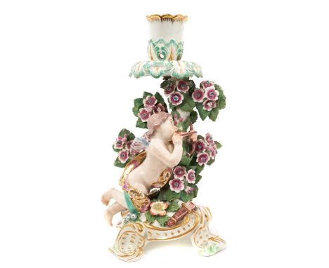 Chelsea candlestick, in the form of Cupid, circa 1765, polychrome decorated, shown kneeling on a floral encrusted scrollwork 