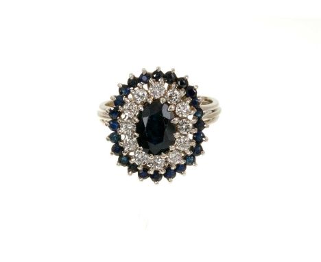 Sapphire and diamond cluster ring with an oval mixed cut blue sapphire surrounded by a border of brilliant cut diamonds and f