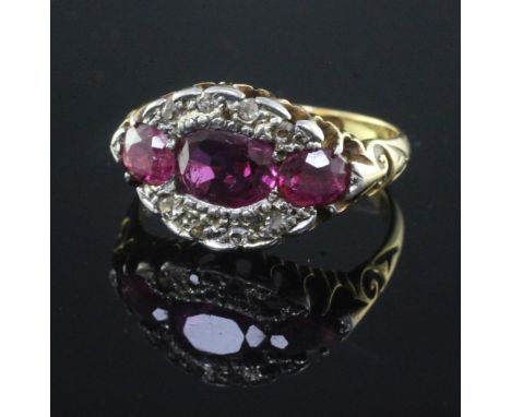 An early 20th century 18ct gold, ruby and diamond oval cluster ring, set with three rubies and surrounded by small diamonds, 