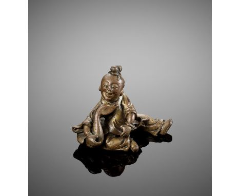 A FIGURAL BRONZE SCROLL WEIGHT, MING DYNASTYChina, 16th - 17th century. Cast in the form of a smiling boy dressed in loose ro